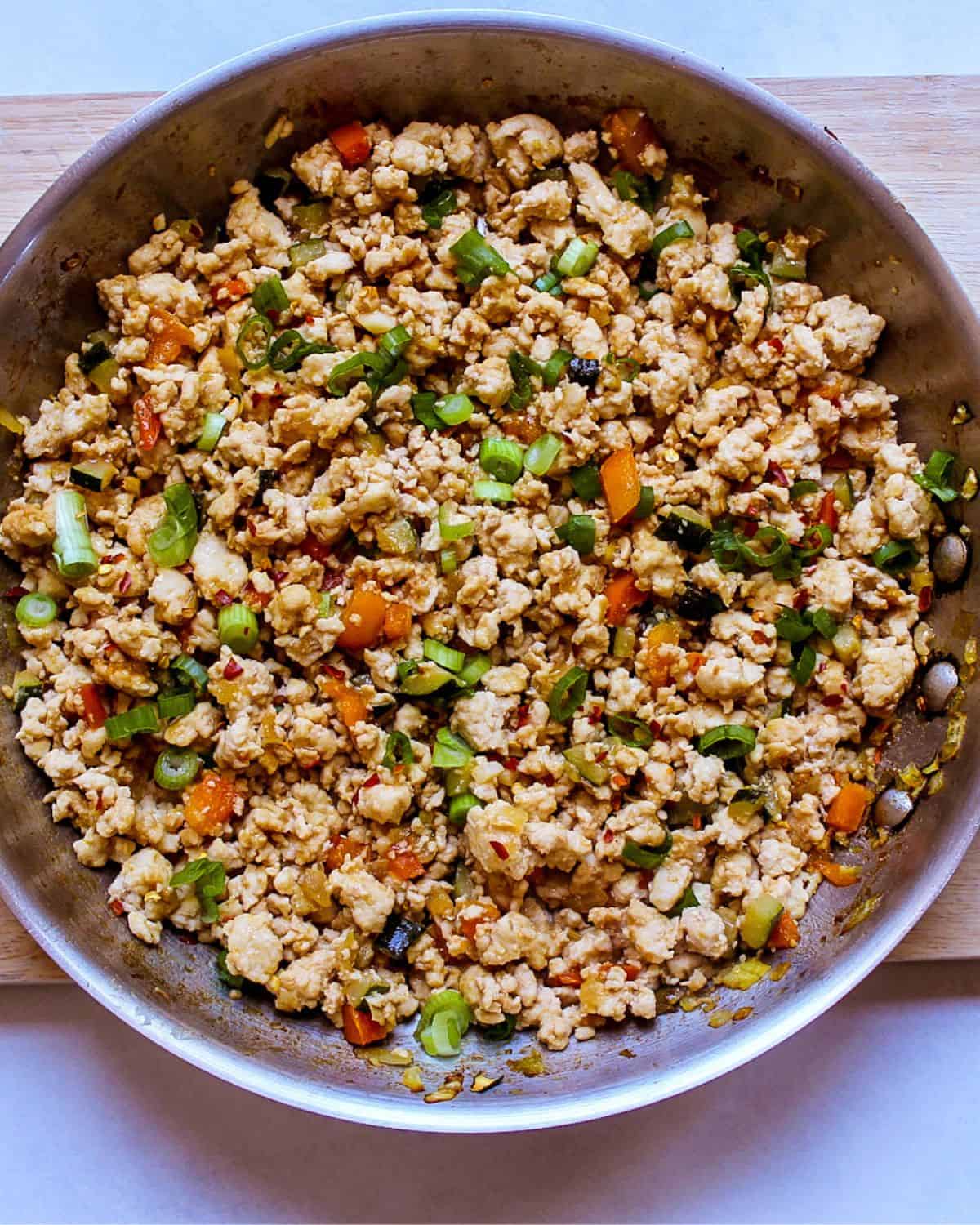 Chicken mince stir fry garnished with green onions in a stainless steel frying pan.