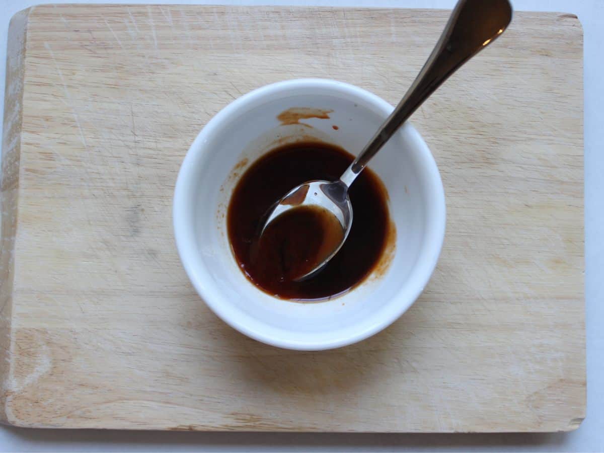 Dark stir fry sauce in a white bowl with a spoon in it.