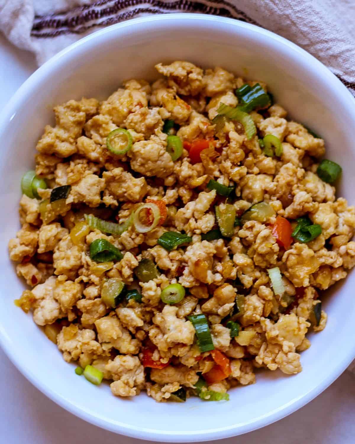 Chicken mince stir fry garnished with green onions in a white bowl.