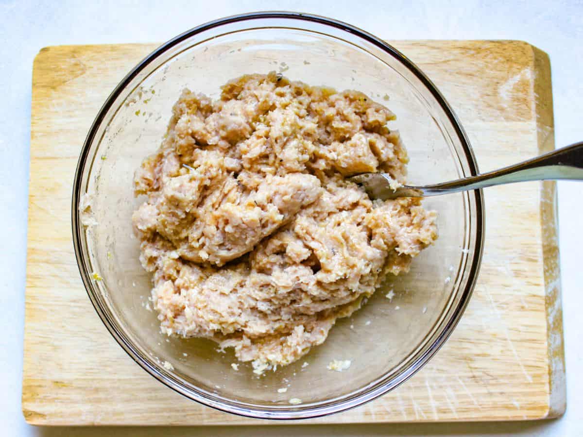 Chicken meat mixture in a glass bowl and a spoon in it.