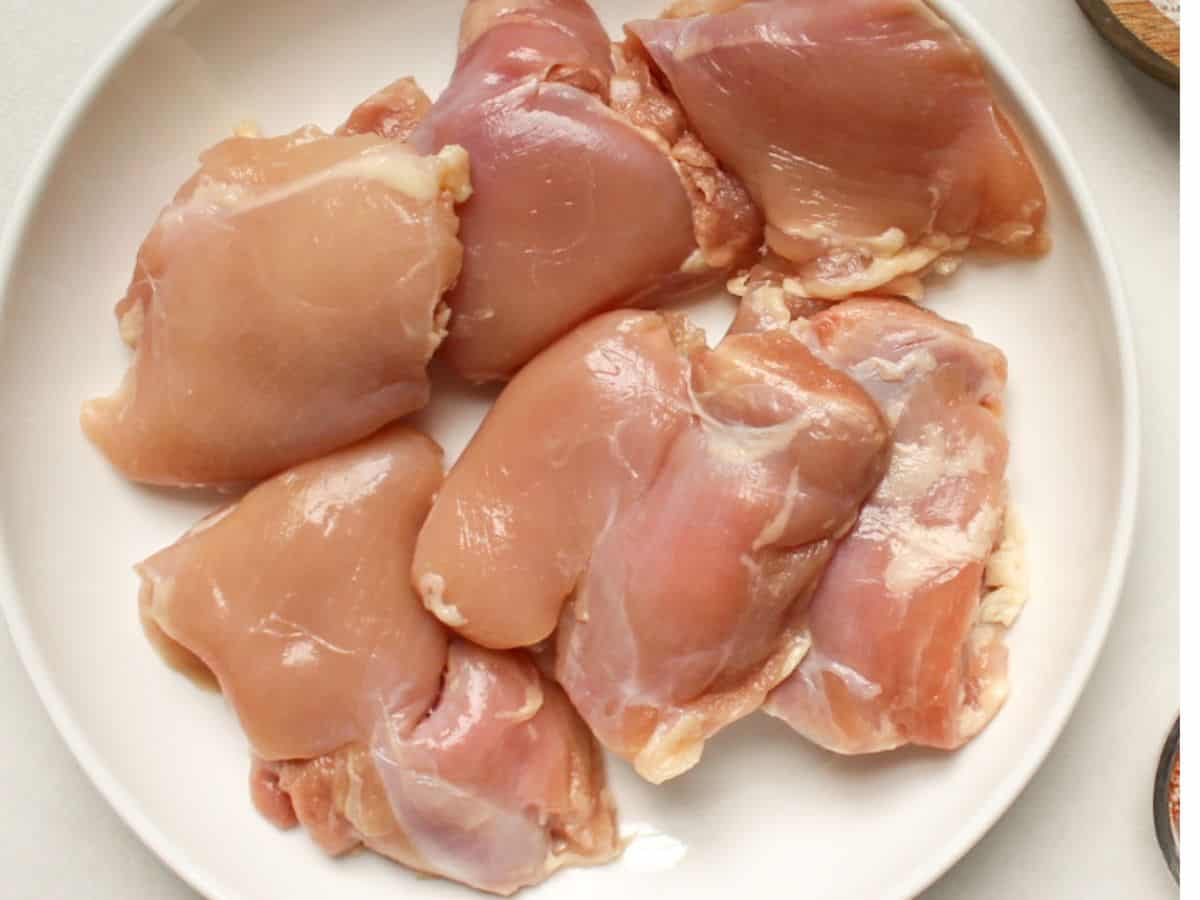 Raw bone-less skinless chicken thighs on a white plate.