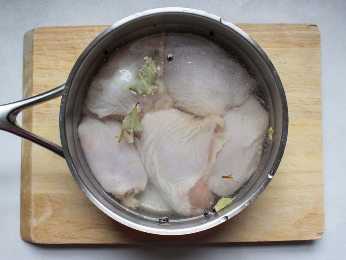Uncooked chicken thighs in a stainless steel pot filled with water.