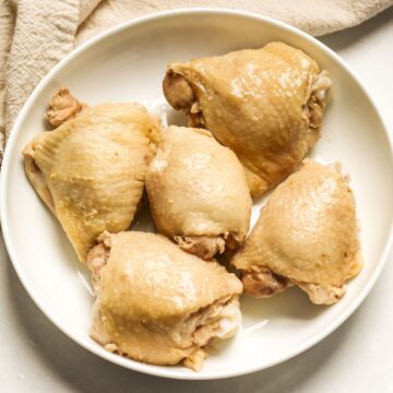 5 boiled skin-on chicken thighs on a white plate.