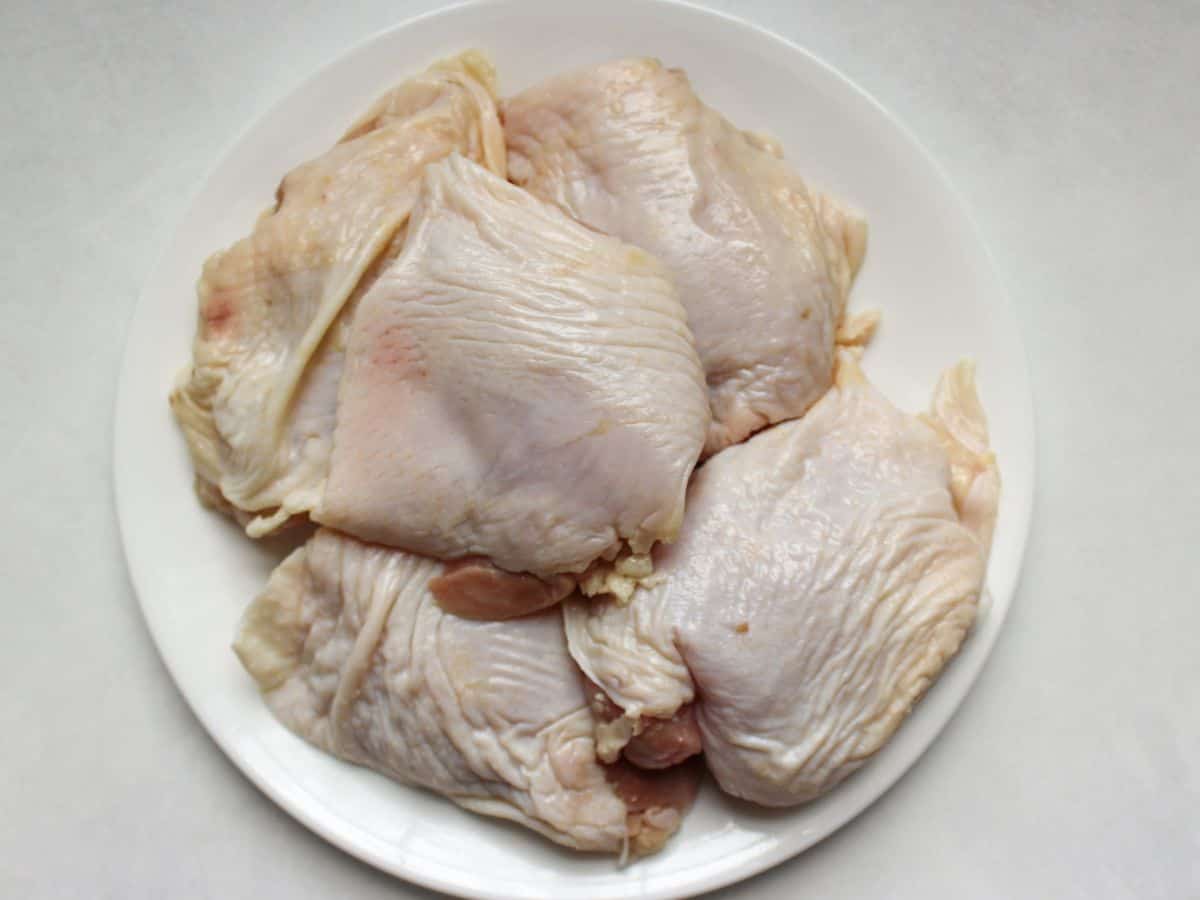 A pile of raw skin on chicken thighs on a white plate.