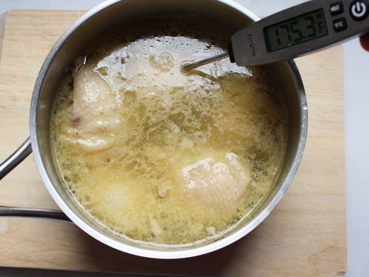 A pot with yellow broth and chicken pieces with a thermometer inserted on one of the thighs showing the recorded temperature of 165.3°F.