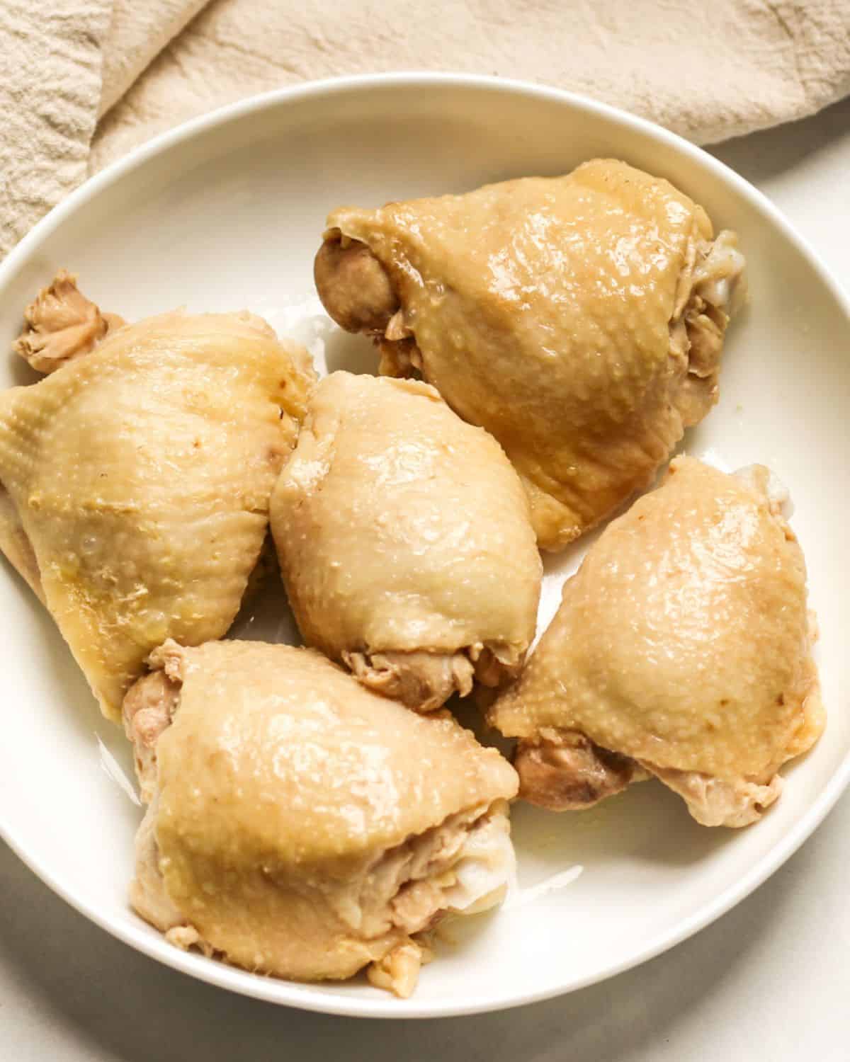 5 boiled skin-on chicken thighs on a white plate.
