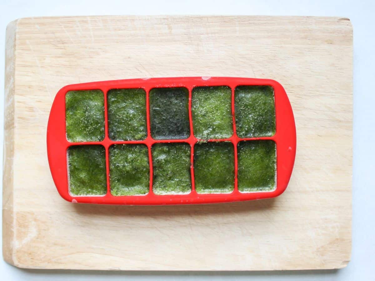 Red ice cube tray filled with frozen pureed greens .