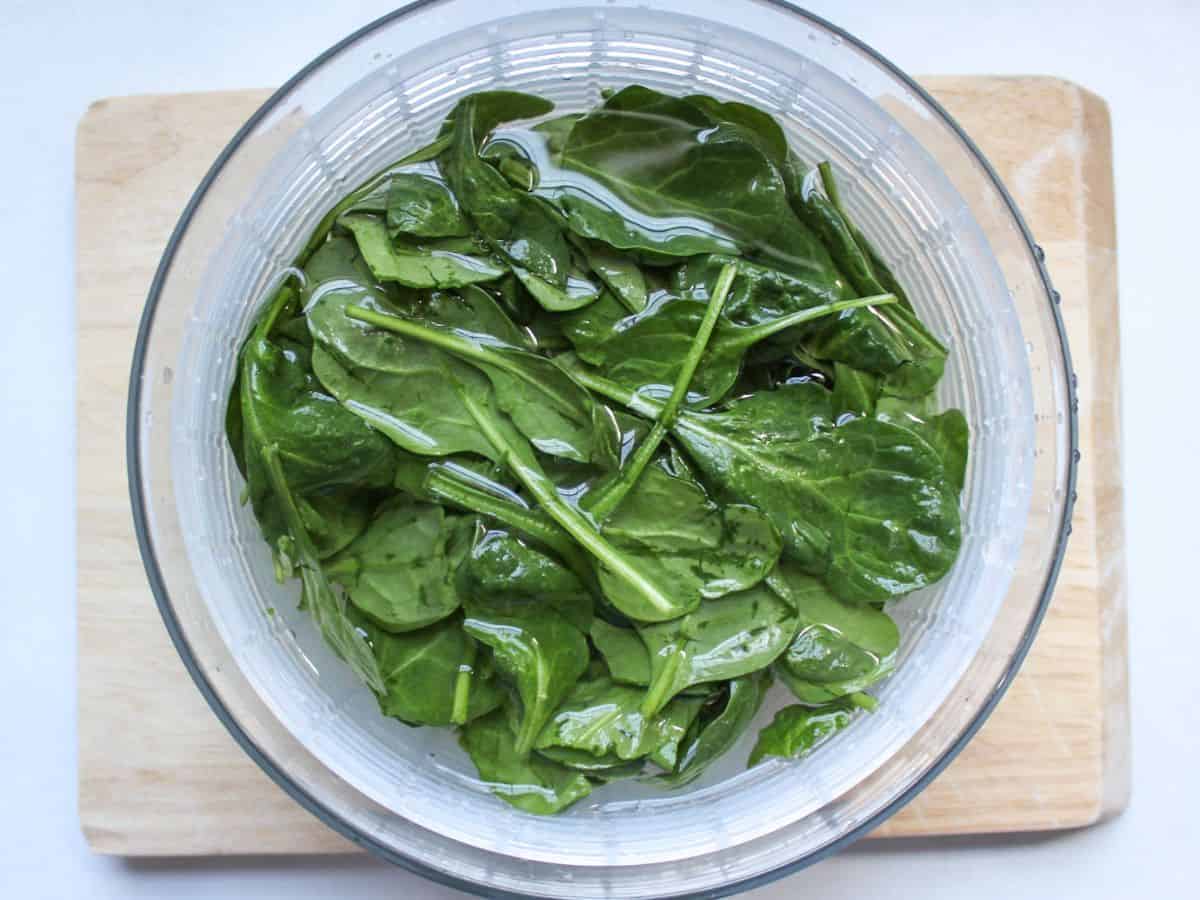 Spinach leaves in a salad spinner bowl filled with water.