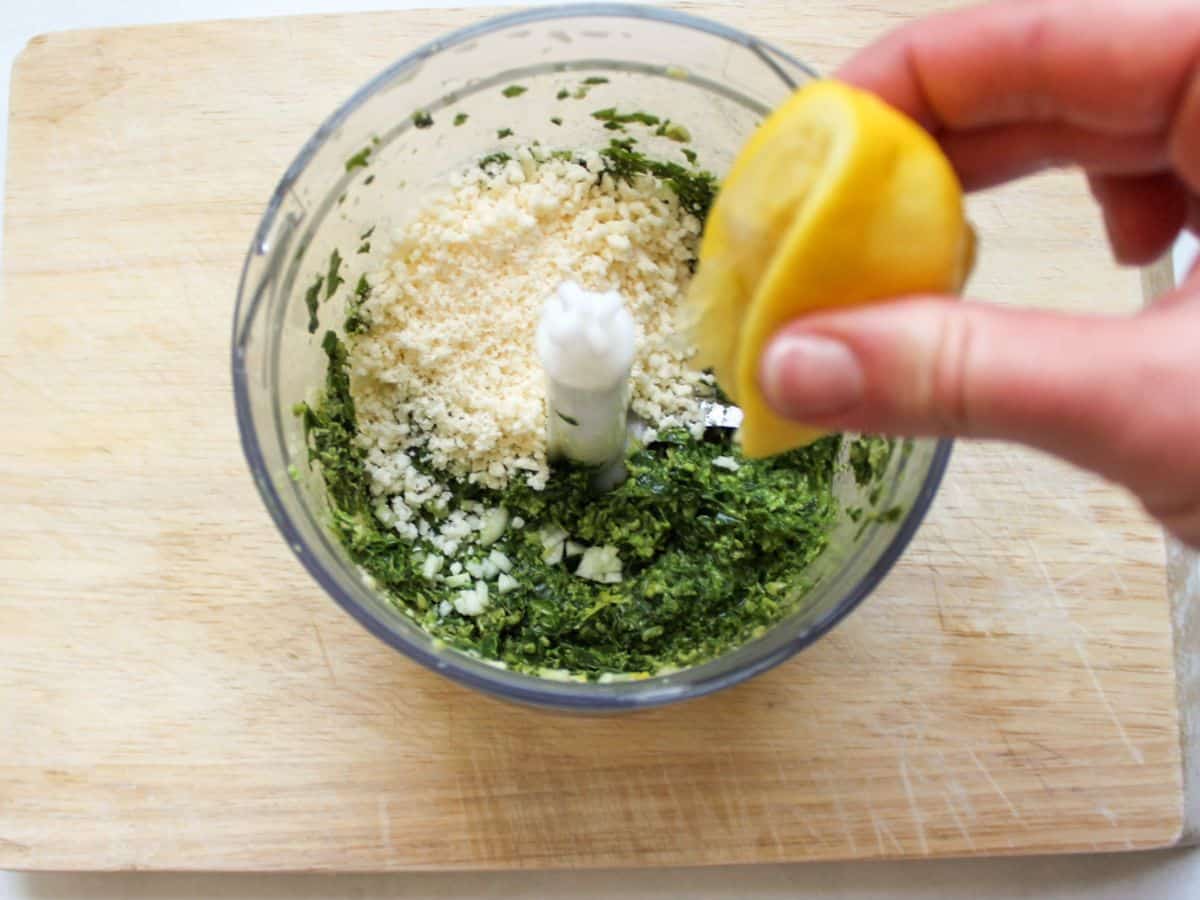 Finely processed green pesto with added grated cheese on top and the lemon being squeezed over it.