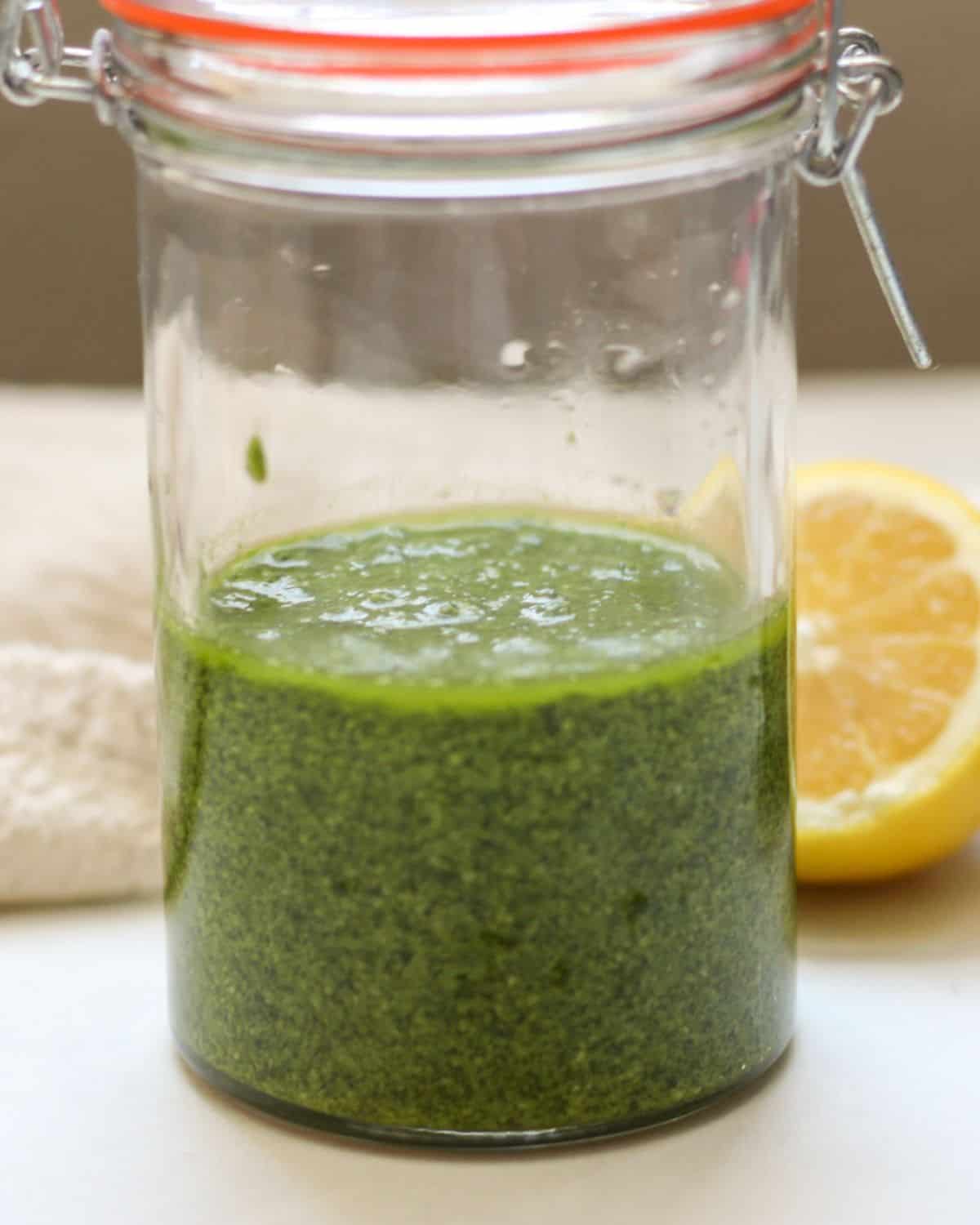 Green sauce in a tall glass jar with the lid.