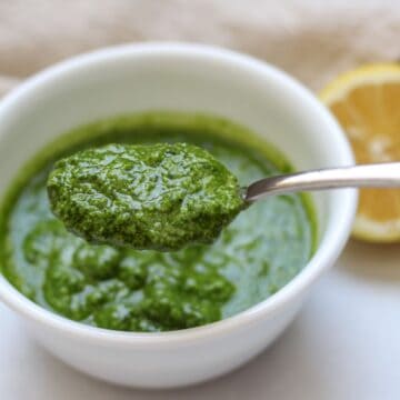Spoonful of lemon pesto over the white bowl that it filled with the rest of the sauce. There is half of the lemon in the background.