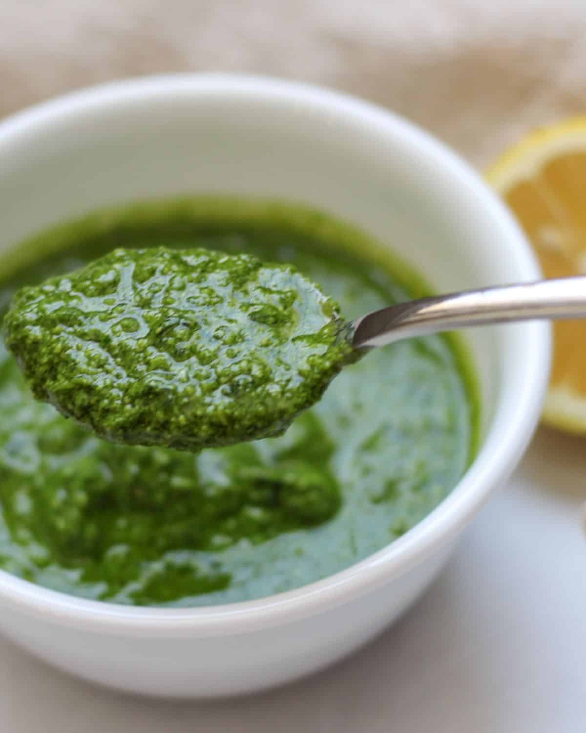 Spoonful of lemon pesto over the white bowl that it filled with the rest of the sauce. There is half of the lemon in the background.