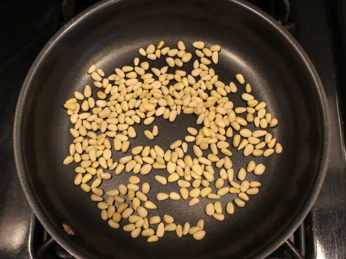 Pine nuts being toasted in a non stick frying pan.