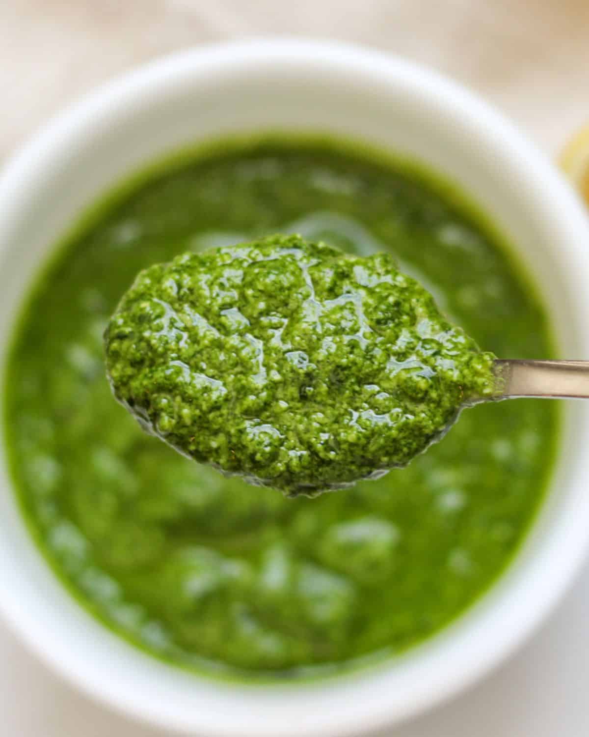 Overhead view of a green peso in a small spoon being held over the white bowl with the remaining green sauce.