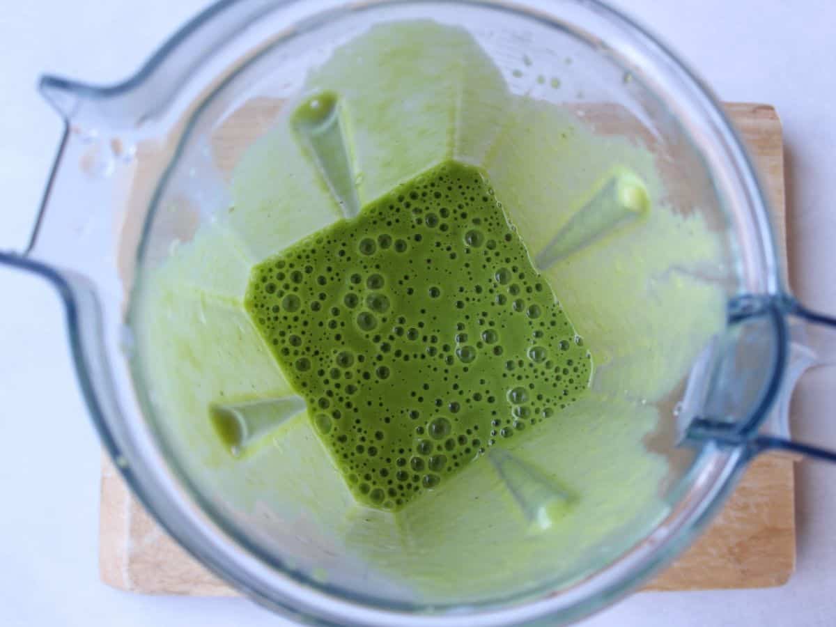 Overhead view of an opened blender container with a green smoothie in it.