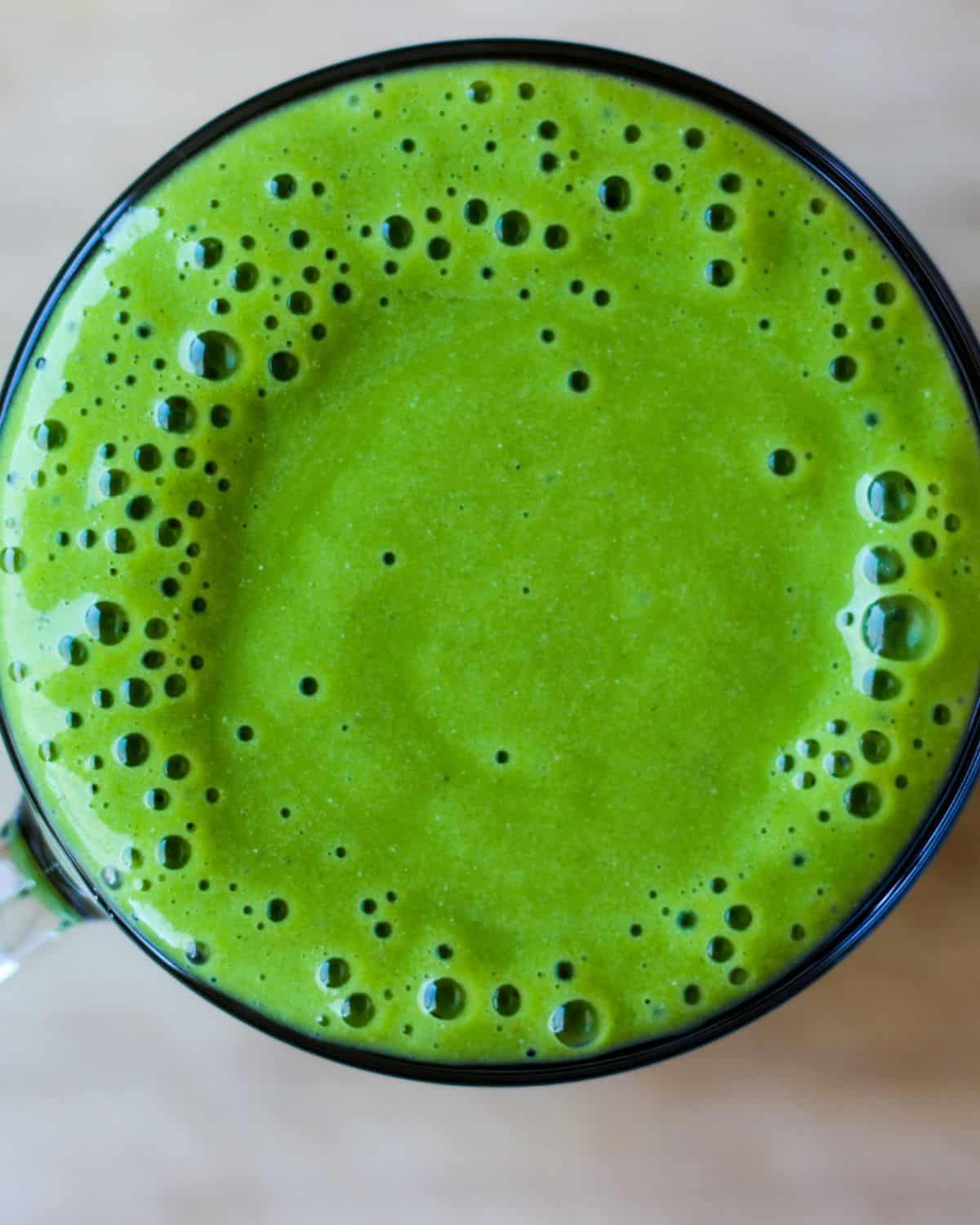 Bright green spinach pineapple smoothie in a glass cup. Overhead view.