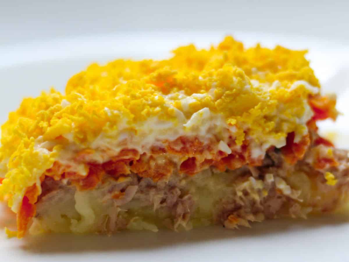 A slice of a layered salad with potatoes ,tuna, carrots and eggs.