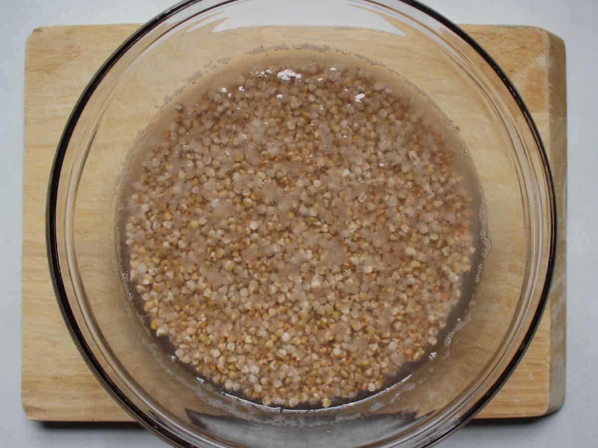 Buckwheat groats soaking in water in a large glass bowl.