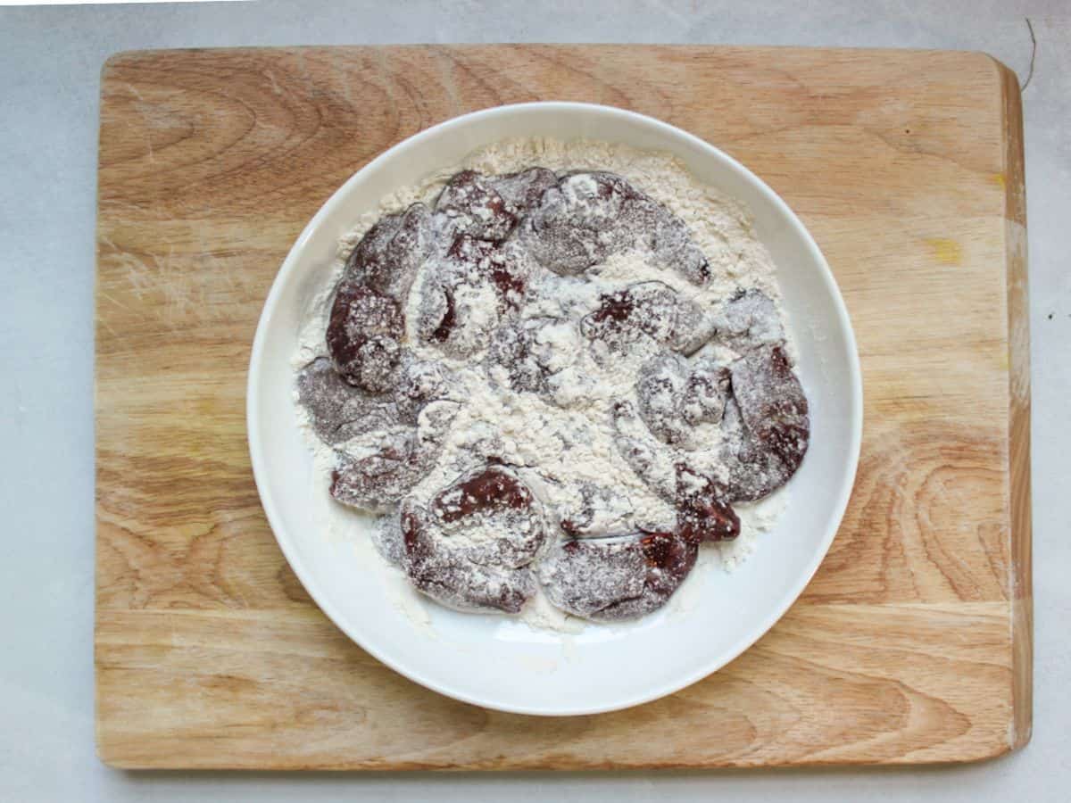 Uncooked chicken liver dredged in flour in a shallow white dish.