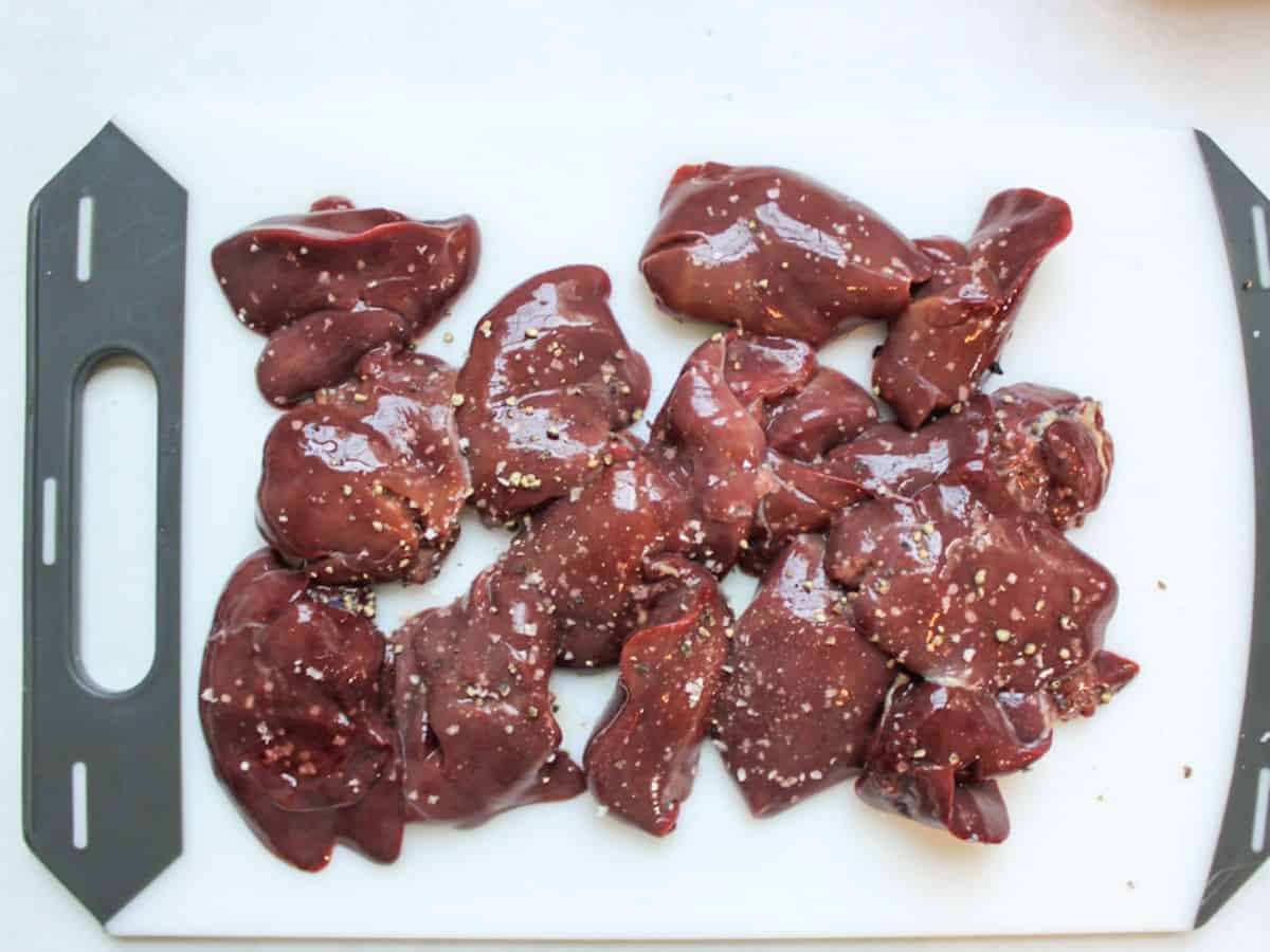 Trimmed raw chicken livers sprinkled with salt and pepper on a white cutting board.