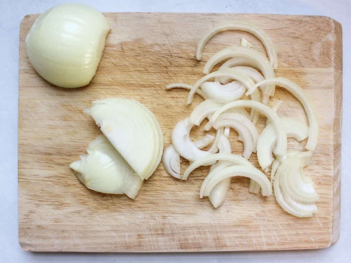 Onion is cut into half rings on a wooden cutting board.
