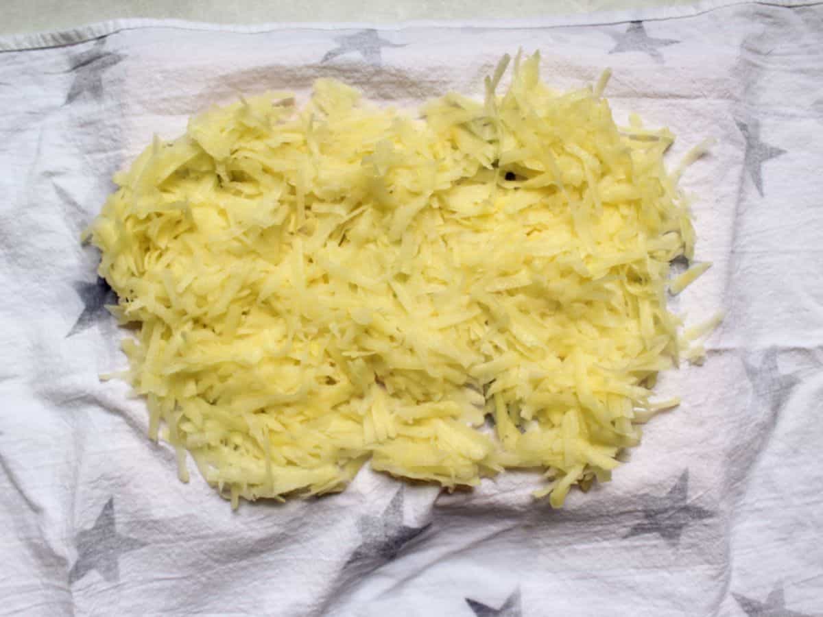 Grated potatoes are spread over the white kitchen towel.