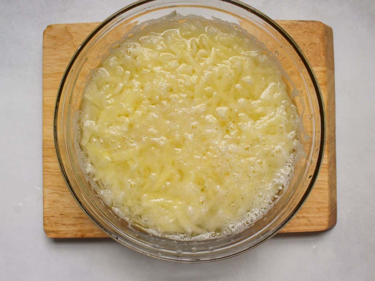 Grated potatoes in a large glass bowl filled with water.