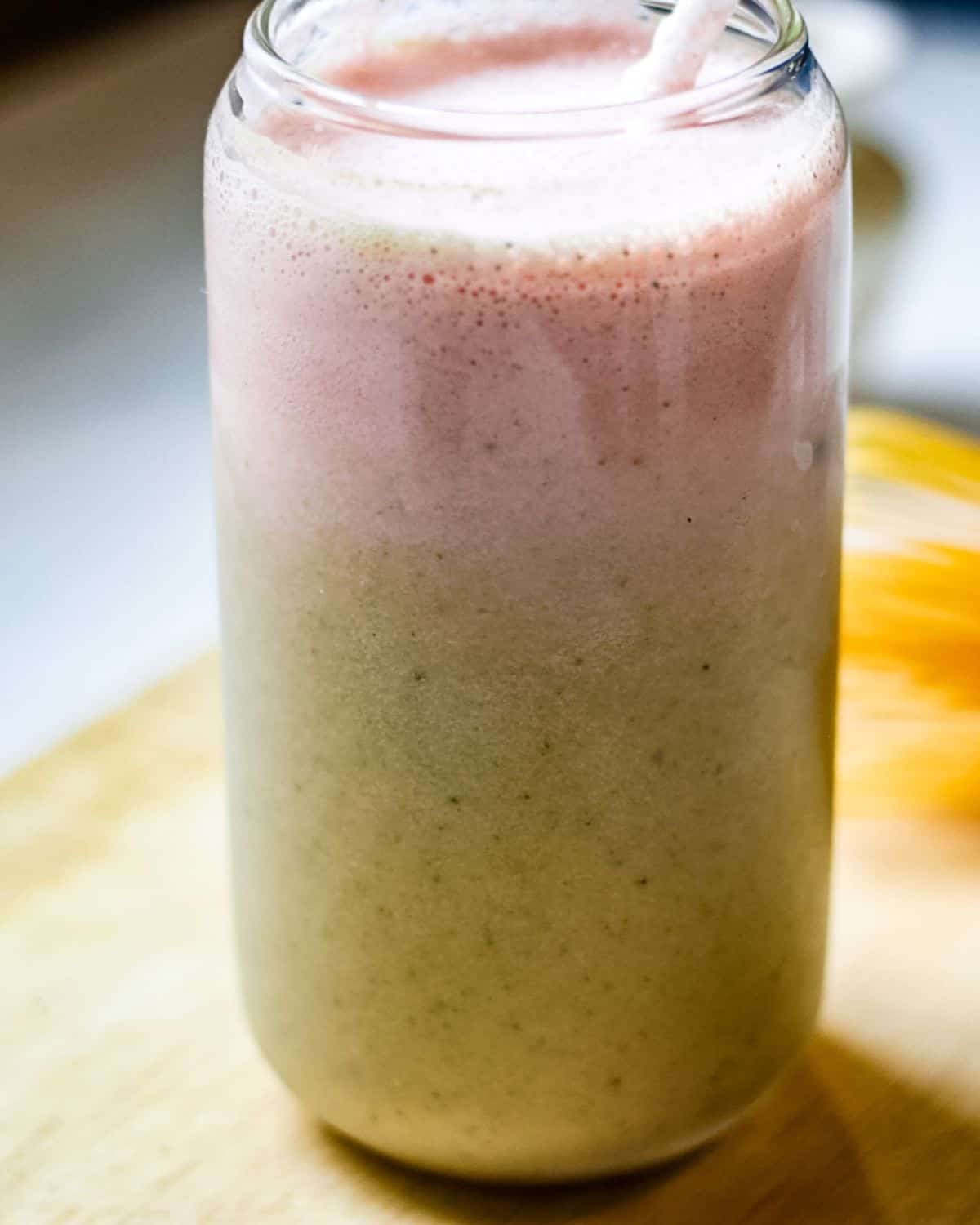 Strawberry matcha latte in a glass with two distinct layers: green at the bottom and pink on top.