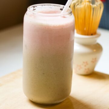 Strawberry matcha latte in a glass with two distinct layers: green at the bottom and pink on top.