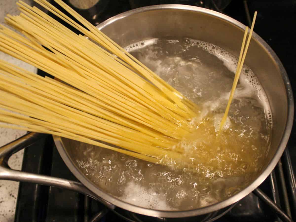 Uncooked spaghetti added to the pot with boiling water.