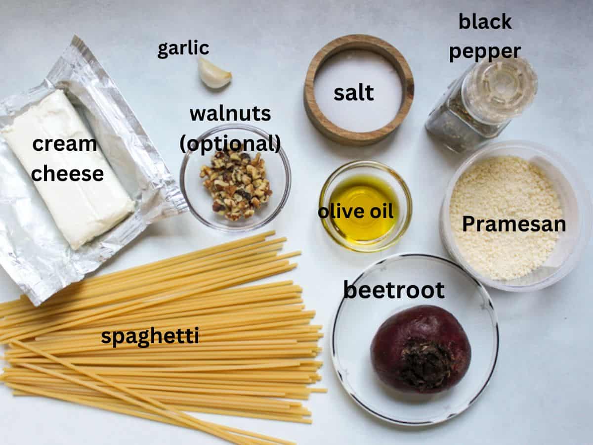 Pasta with beet sauce ingredients on a white background: spaghetti, cream cheese, garlic, walnuts, olive oi, salt, beetroot, grated Parmesan, black pepper.