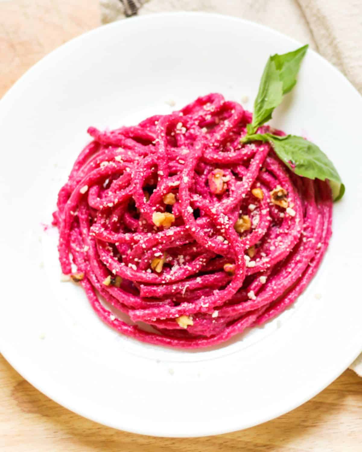 Overhead view of pink pasta with walnuts, grated Parmesan and two basil leaves on top.
