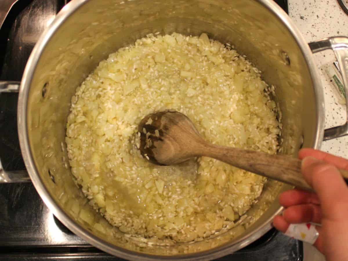 The broth added to the rice in a pot with a wooden spoon in it.