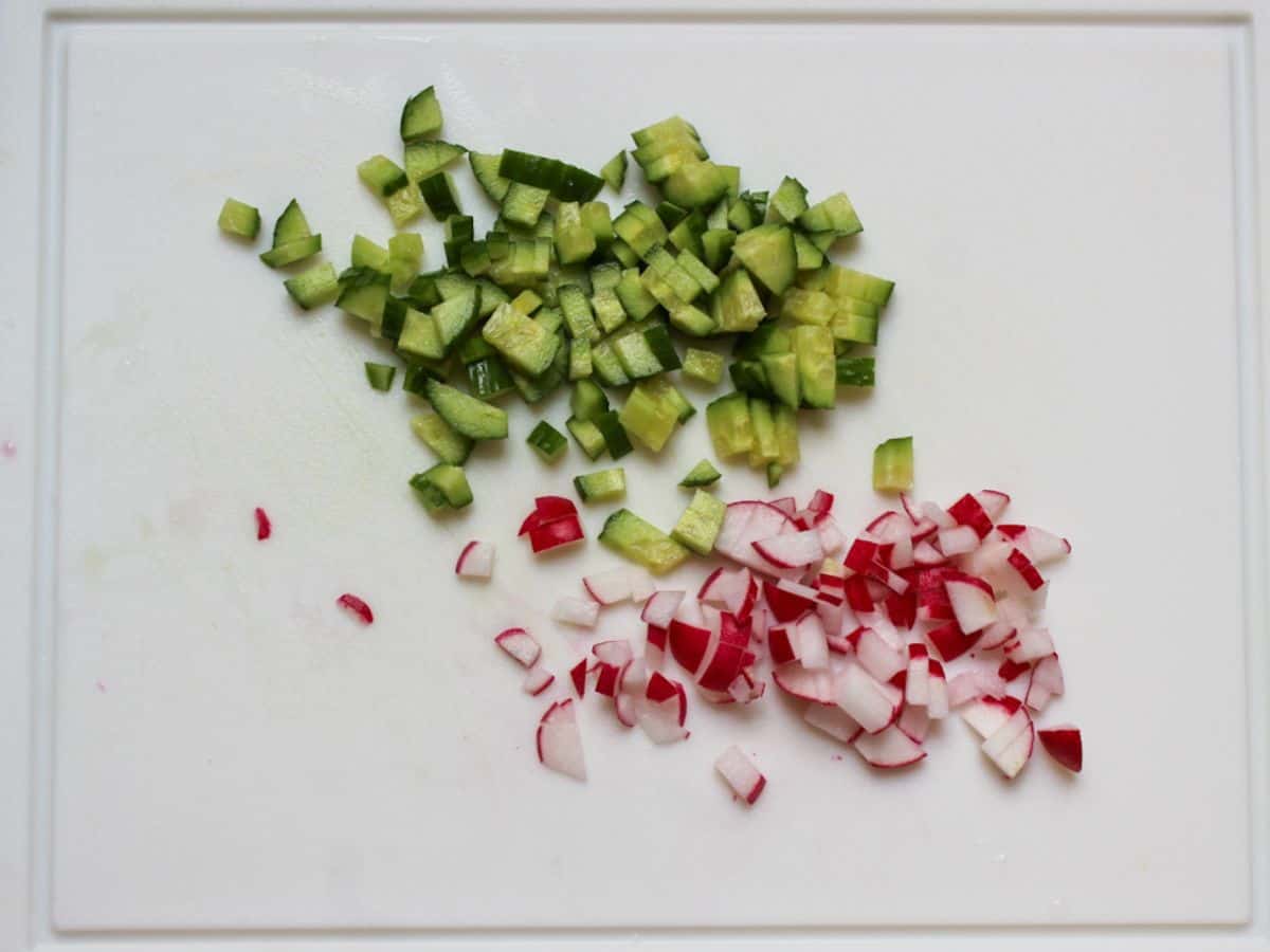 Diced into small pieces cucumbers and red radishes on a cutting board.