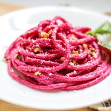 Beetroot spaghetti served on a white plate is topped with walnut pieces and grated Parmesan cheese.