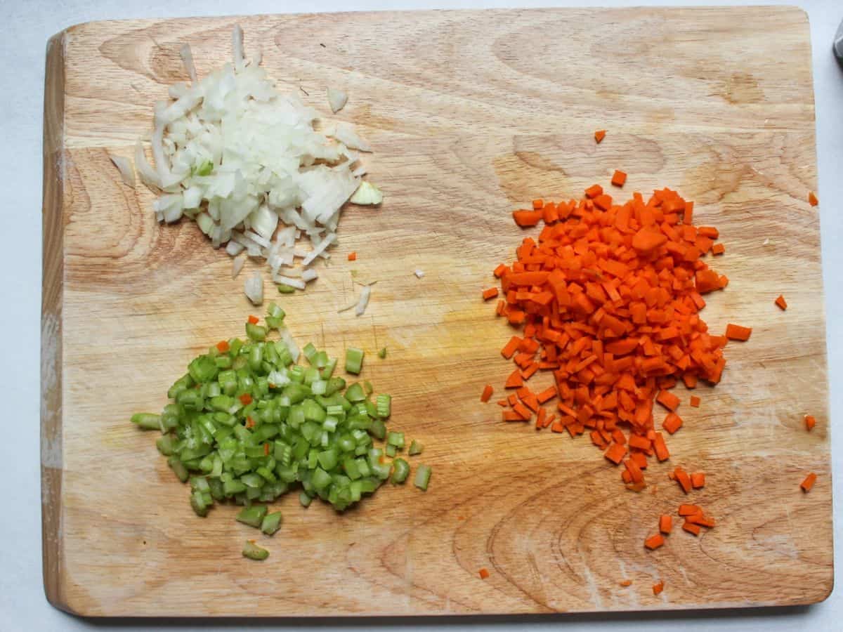 Diced onions, diced celery and diced carrots on a wooden cutting board.