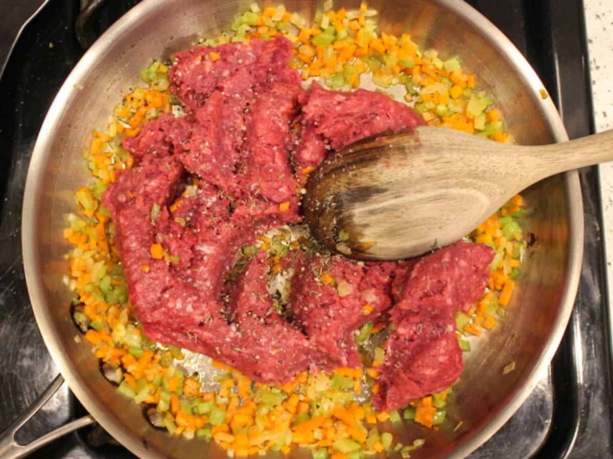 Raw ground beef added to the skillet with sauteed vegetables.