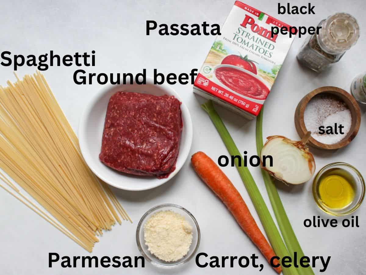 Recipe ingredients on a white background: spaghetti, ground beef, passata, carrot, celery, onion, olive oil, salt, black pepper, grated Parmesan.