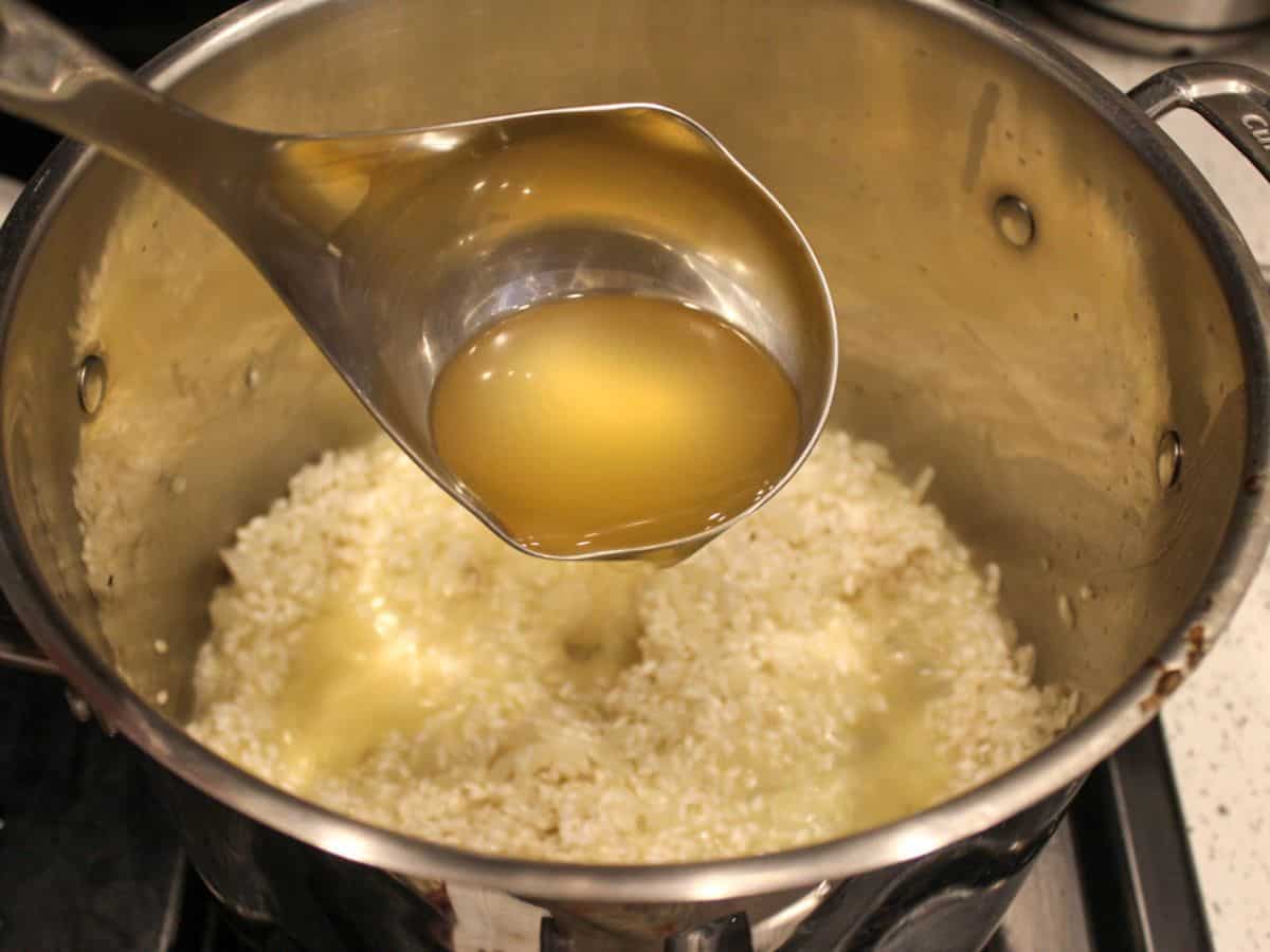 A ladle filled with broth poured into the pot with risotto.