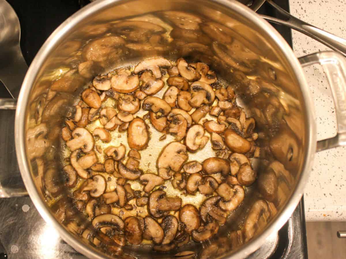 Sliced baby bella mushrooms sauteing in the stainless steel wide pot.