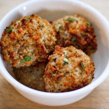 Air fried risotto arancini balls in a white bowl garnished with pieces of green parsley.