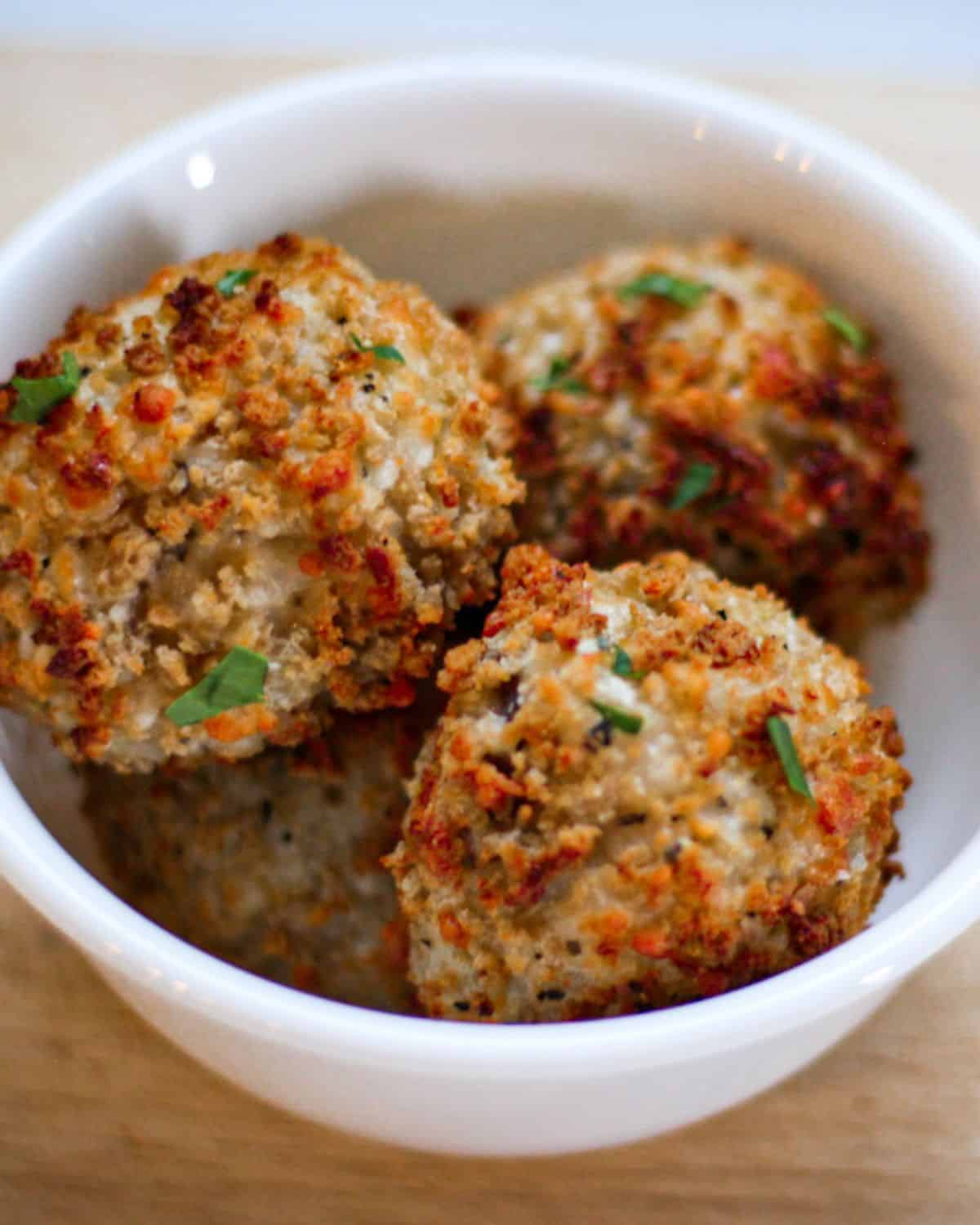 Air fried risotto arancini balls in a white bowl garnished with pieces of green parsley. 