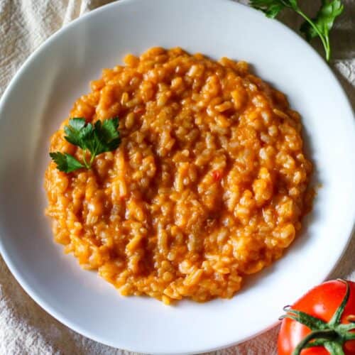 Risotto al pomodoro in a white shallow dish garnished with a leaf of fresh green parsley.