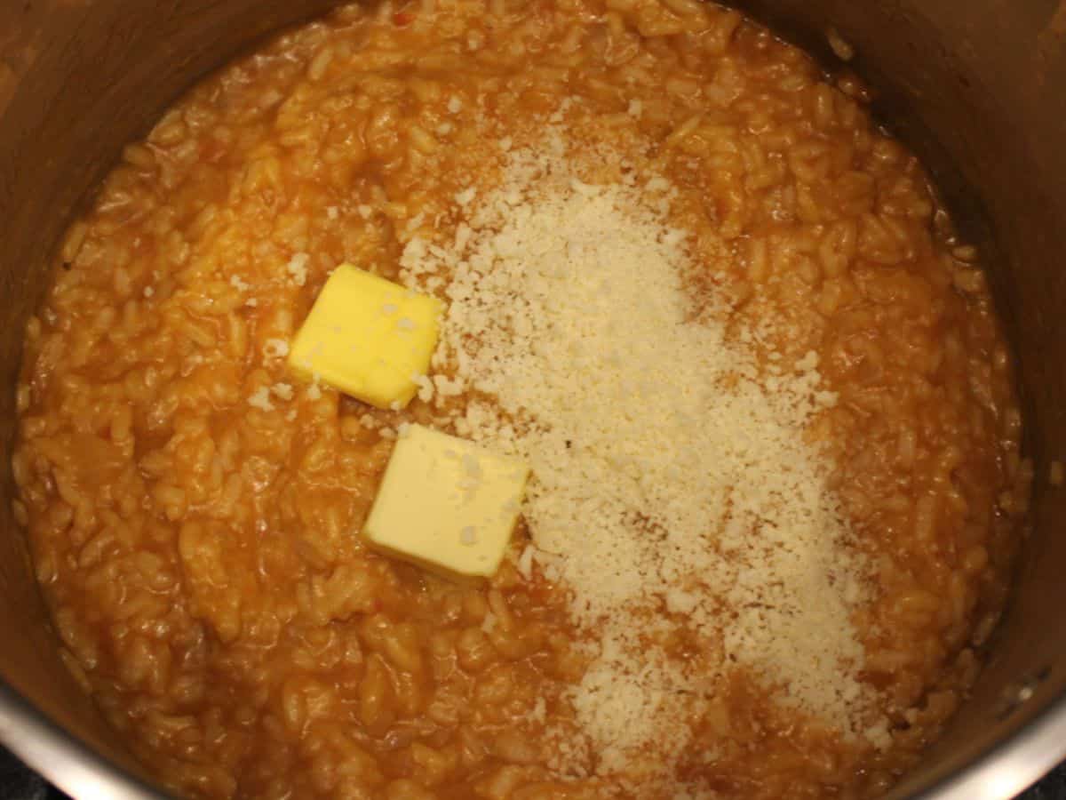 Butter and grated Parmesan cheese added to the cooked tomato risotto in a pot.
