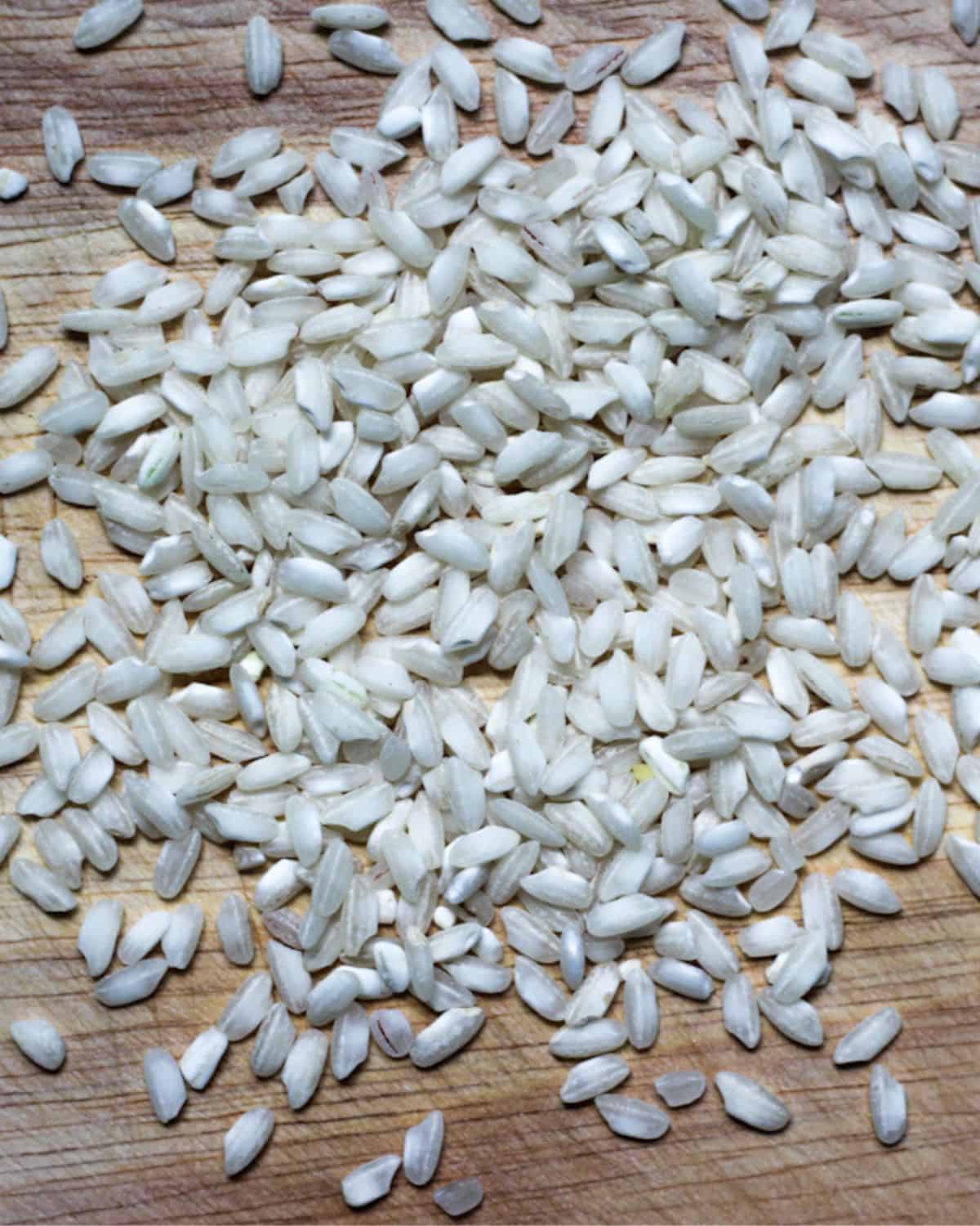 Uncooked Arborio rice grains poured over the wooden surface.