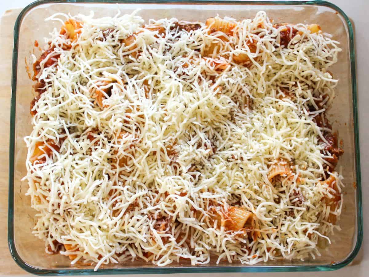 Shredded mozzarella on top of the pasta in a rectangular glass baking dish.