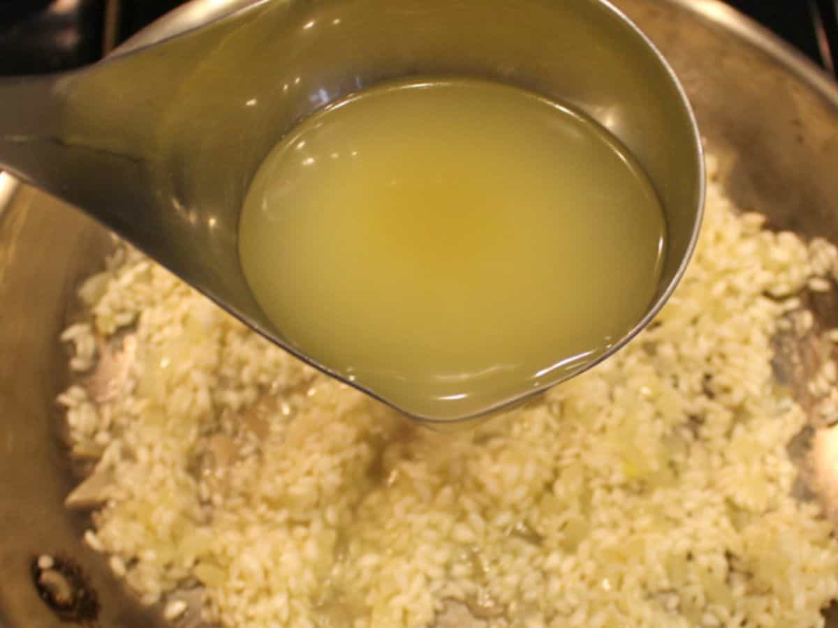 Adding a ladle with chicken broth to the rice.