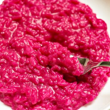 Pink beetroot risotto in a white dish with a fork scooping the risotto.