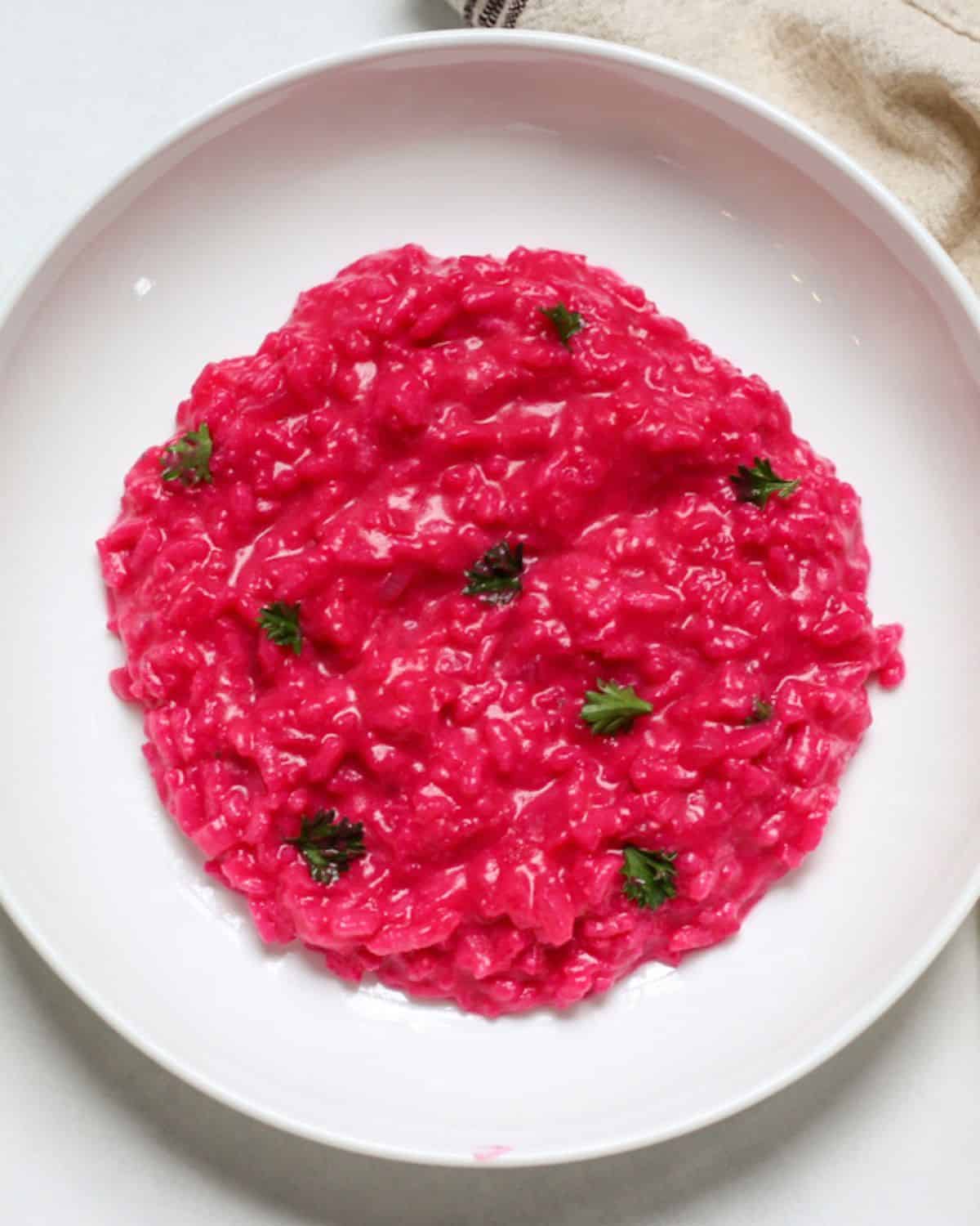 Pink-colored risotto in a shallow white dish garnished with fresh green parsley.