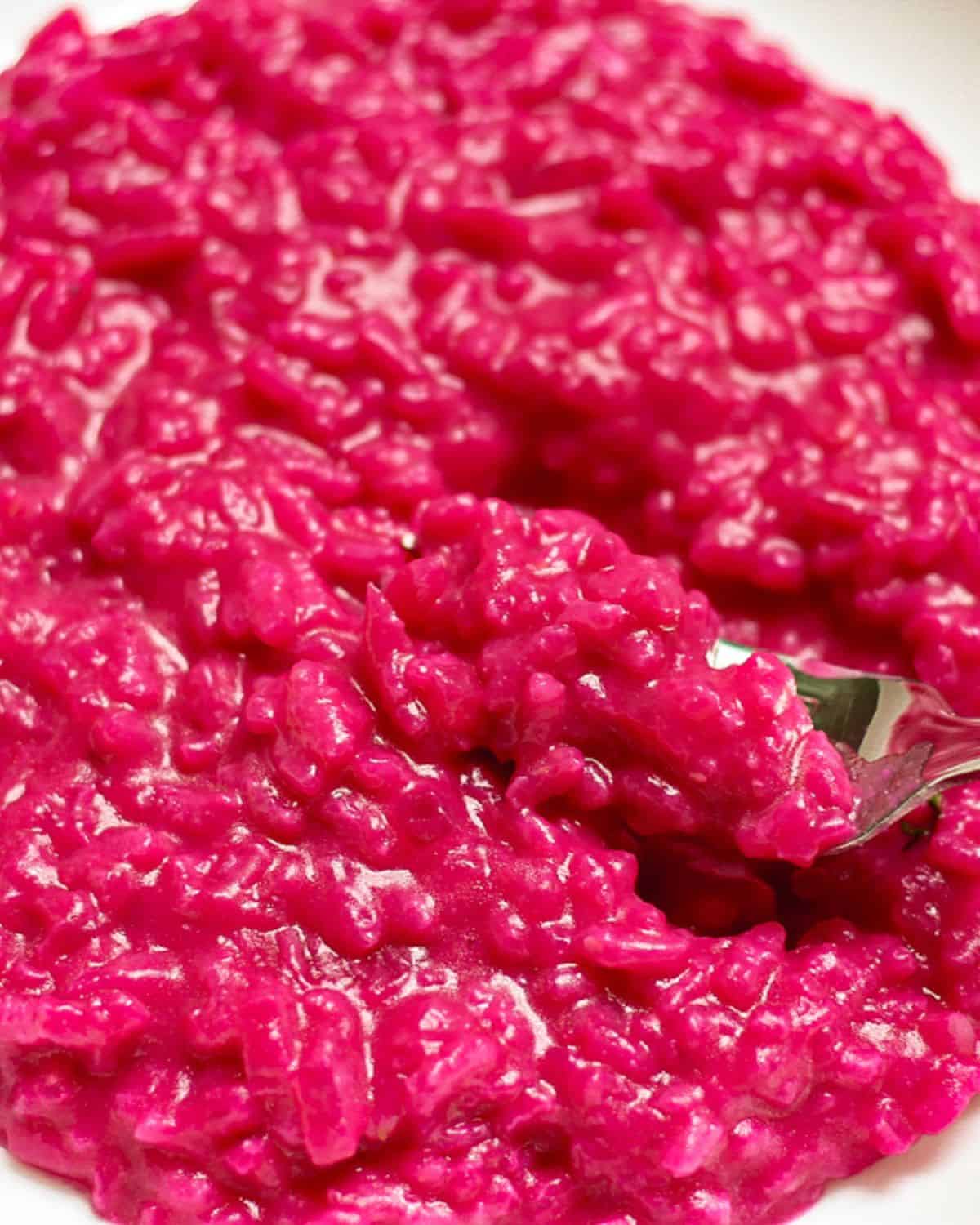 Pink beetroot risotto in a white dish with a fork scooping the risotto.